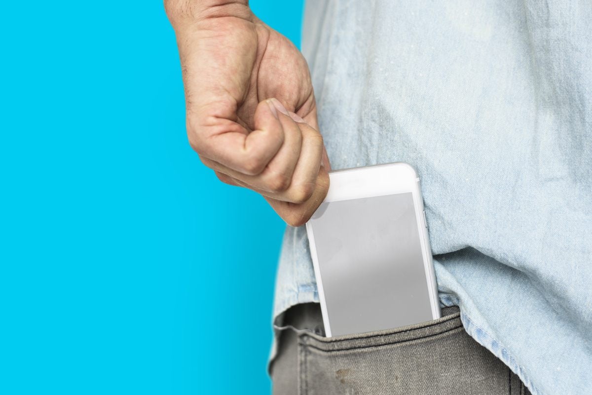 Man placing his phone in his back jeans pocket, with an aqua blue background