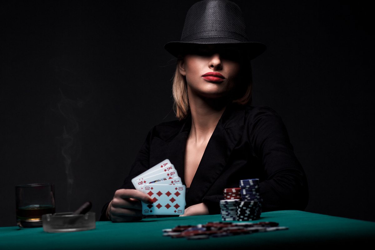 Woman wearing a black hat, holding a royal flush in her right hand