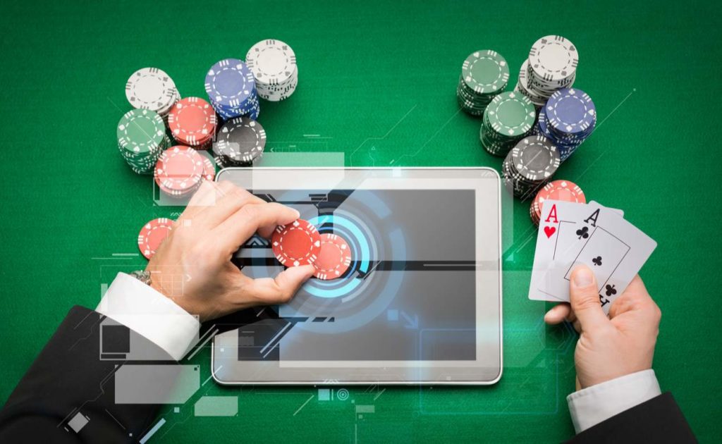 Close up of poker player with playing cards, tablet device and chips at green casino table