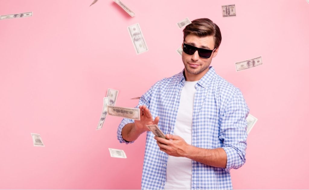 Portrait of trendy carefree man surrounded by money isolated over pink pastel background