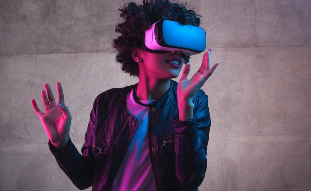 Cheerful girl with hands up wearing virtual reality goggles.
