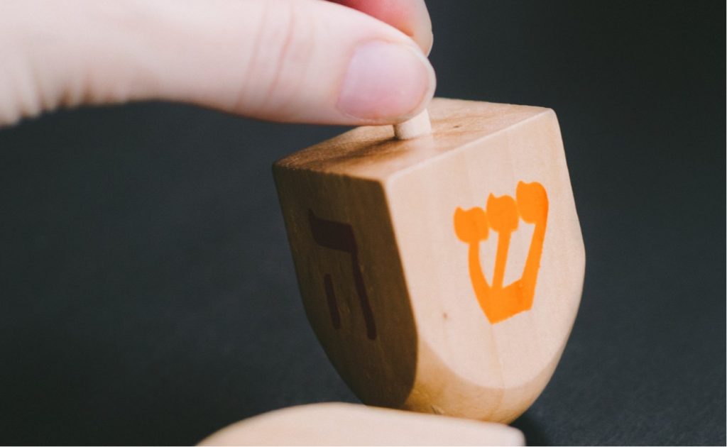 A Dreidel in hand with the "shin" character facing out before being spun