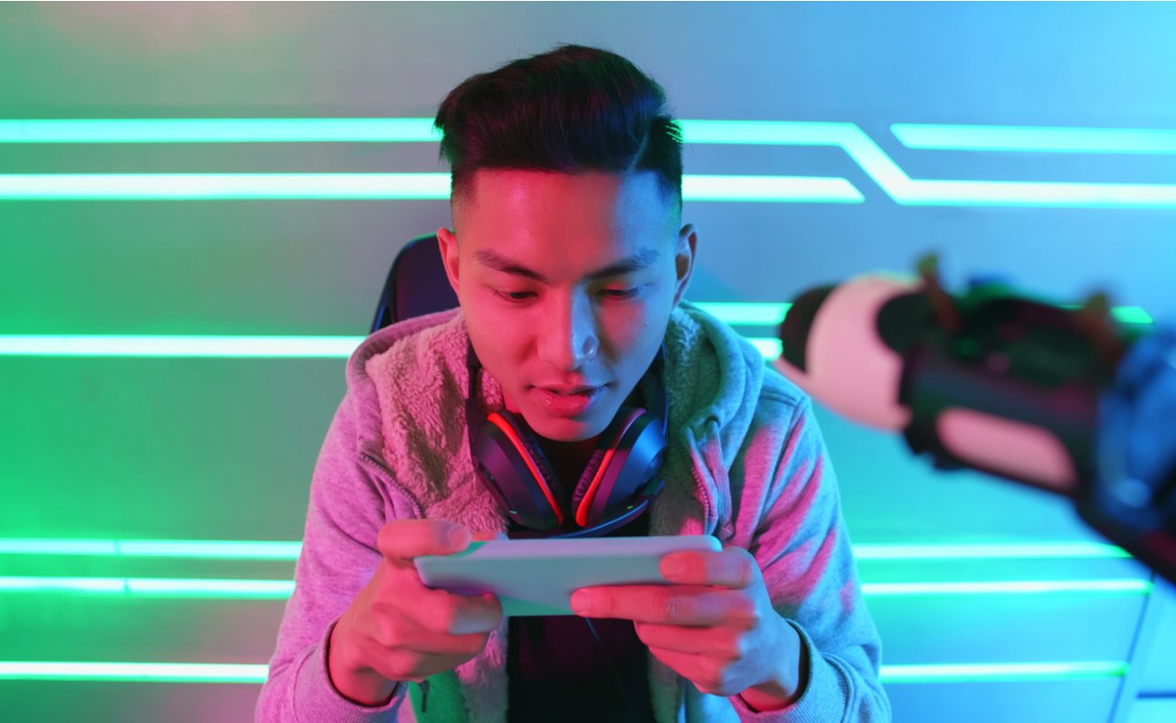 A young man with headphones around his neck is focused on his mobile game