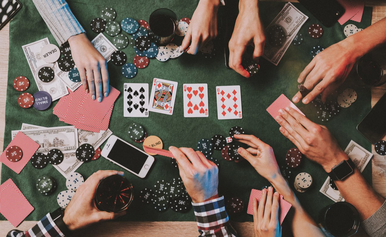 A group of people playing a casual poker game, with cards and casino chips on a green felt table.