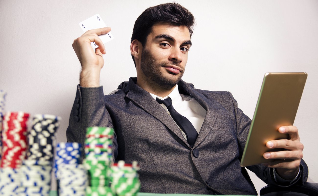 Elegant man in a suit holding the ace of spades and a tablet with stacks of poker chips in the foreground.
