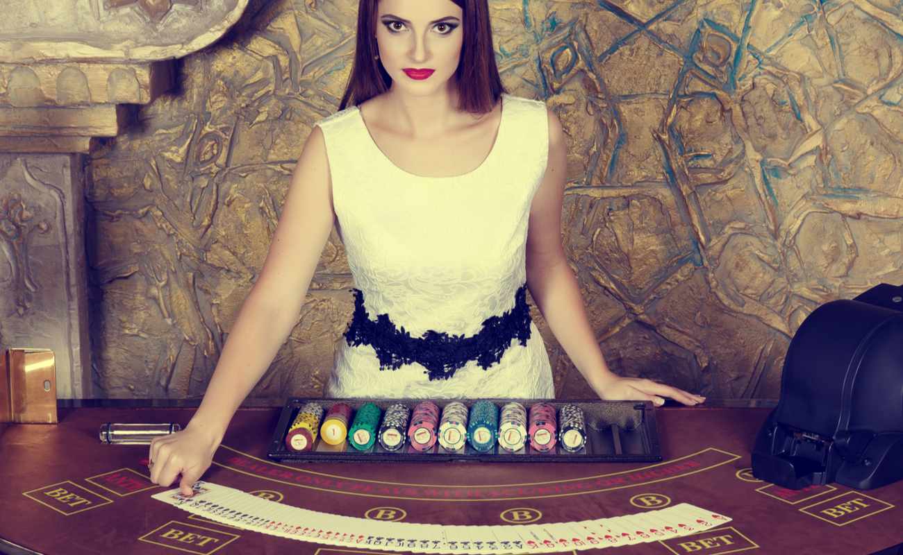 A female dealer stands at a decorated casino table with playing cards and casino chips.