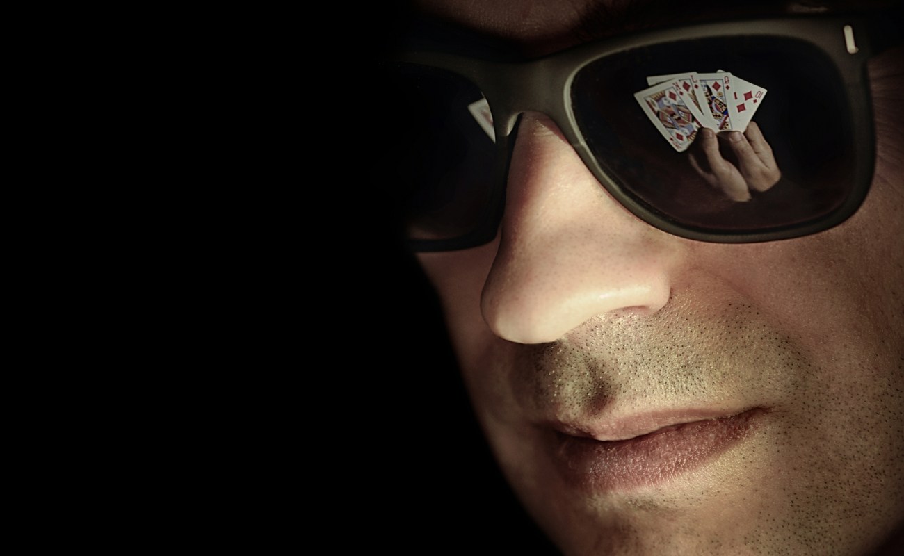 Man with sunglasses with the lenses reflecting playing cards he is holding in his hands.