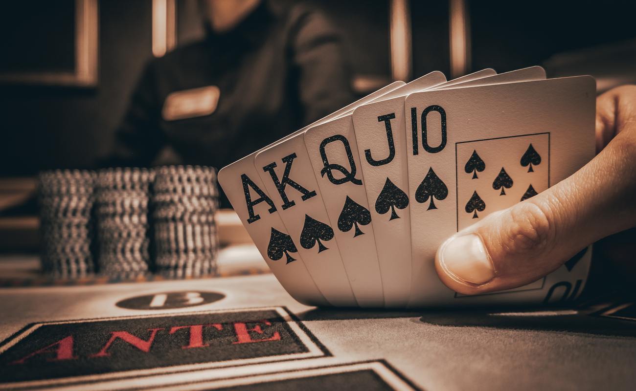 A royal flush of spades on a casino table with poker chips and the dealer in the background.