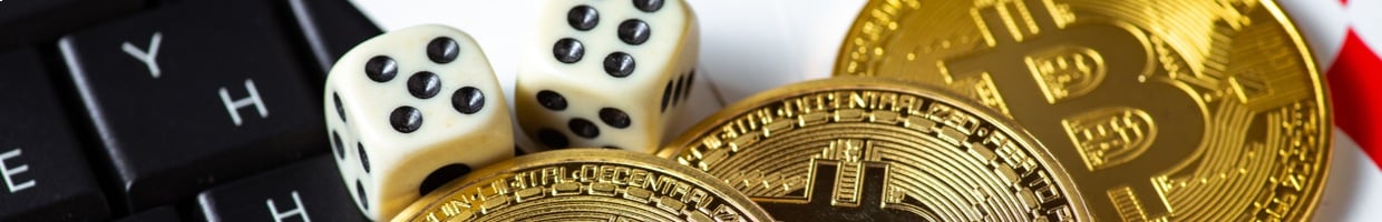 three coins representing cryptocurrency sit on a keyboard next to a pair of dice and some playing cards.