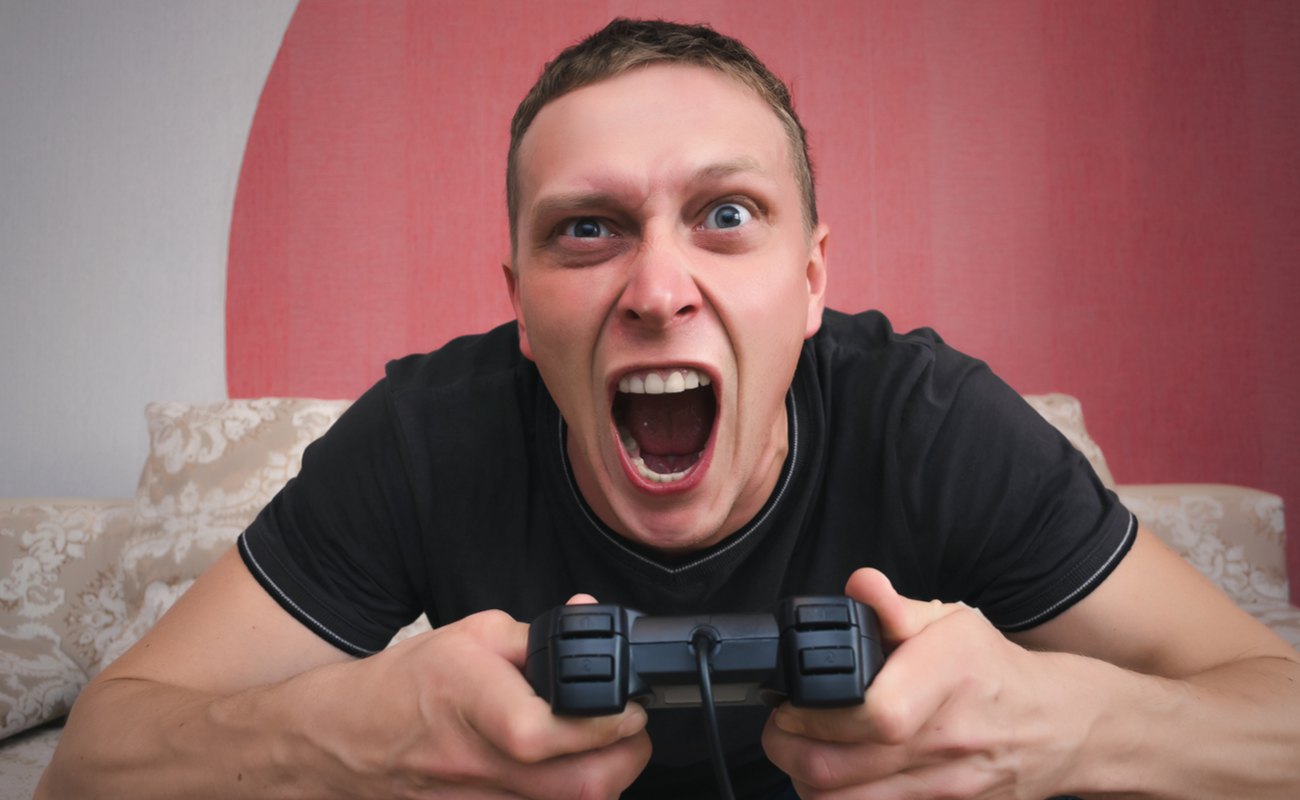 A man sitting on a couch with a controller in his hand screams at the TV.