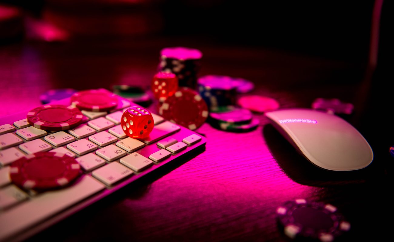 A keyboard and mouse covered with dice and casino chips.