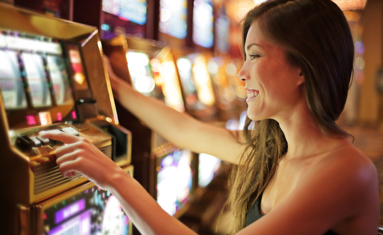 A happy woman playing a slot machine at a land-based casino.
