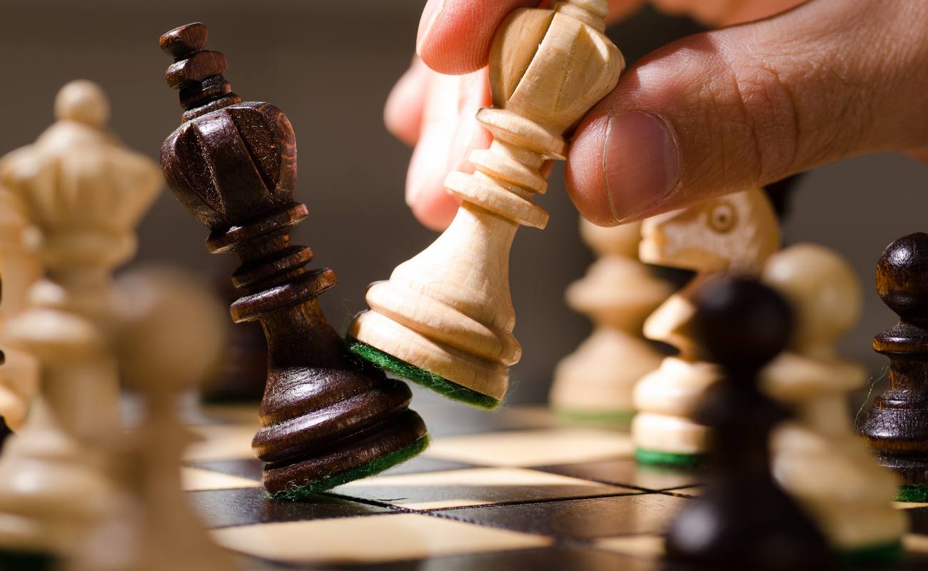 A hand with a chess piece knocks over an opponent’s king, indicating ‘checkmate.’