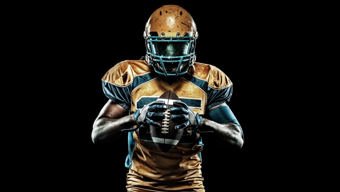 An American football player holds a football between his hands.