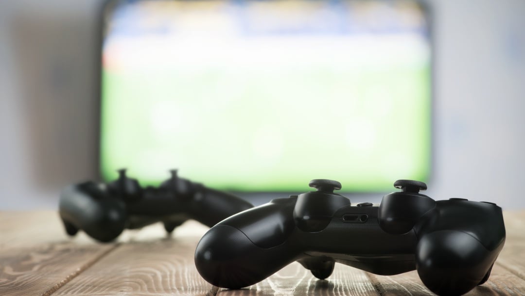 Video game consoles on a wooden surface and a TV in the background.