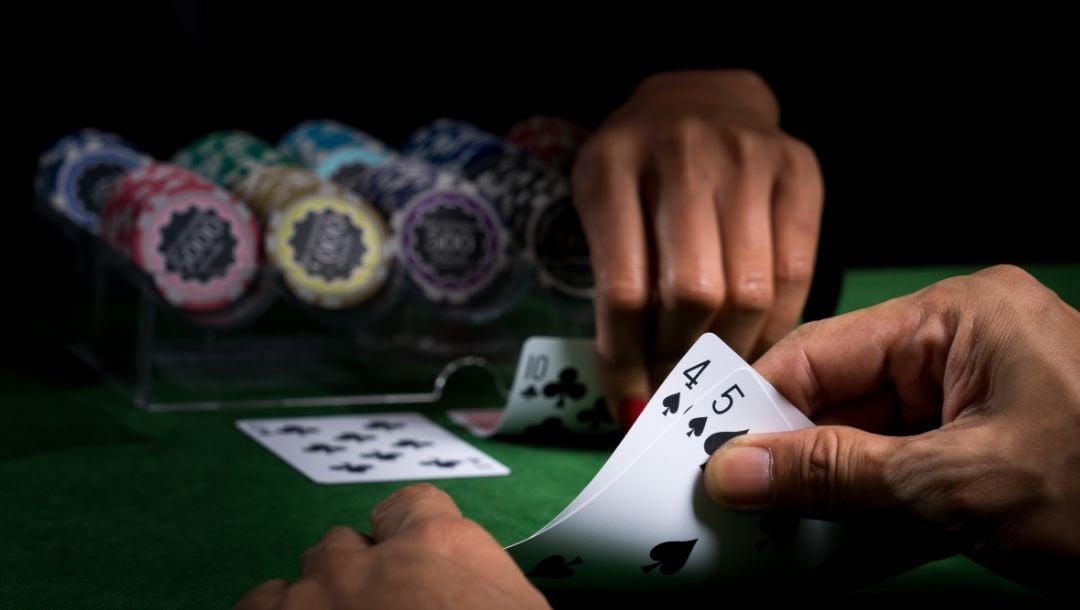 a man checking his hole cards at a green felt casino table opposite the croupier