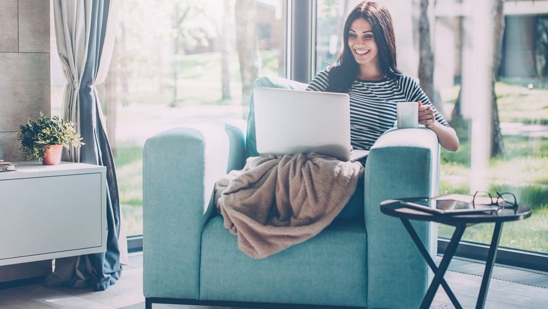 A women drinking coffee while looking at her laptop.