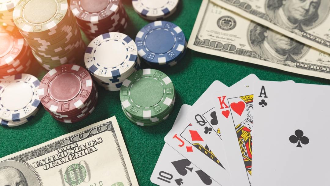 A casino table with stacks of casino chips, $100 notes and a flush poker hand spread out.