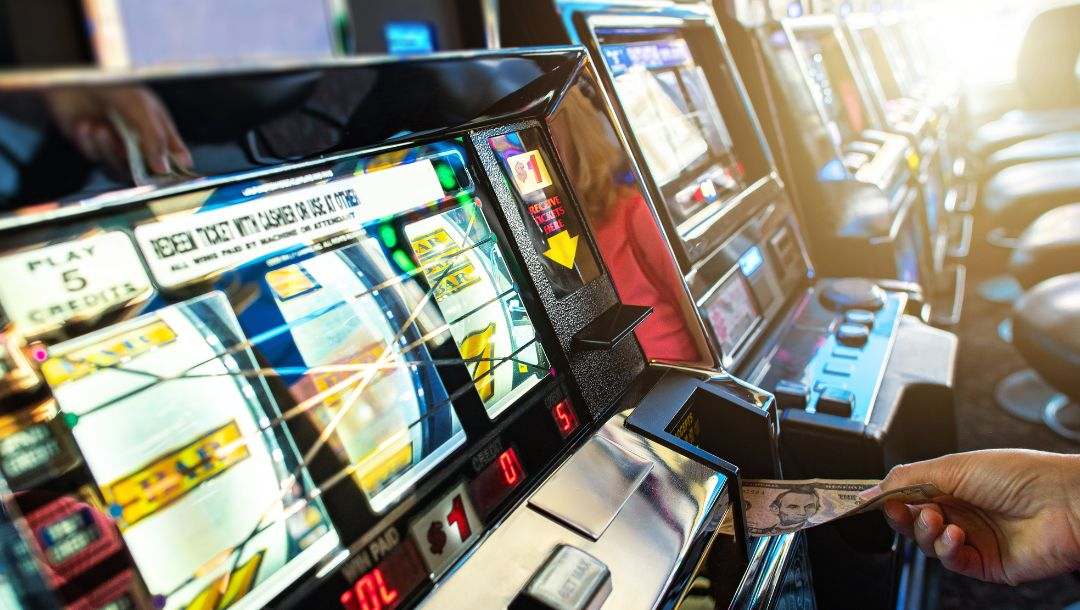 A person putting money into a slot machine at a casino.