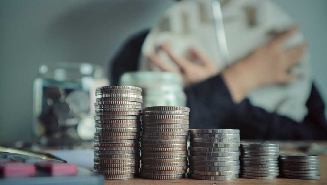 A row of coins in the foreground and a person holding a clock in the background.