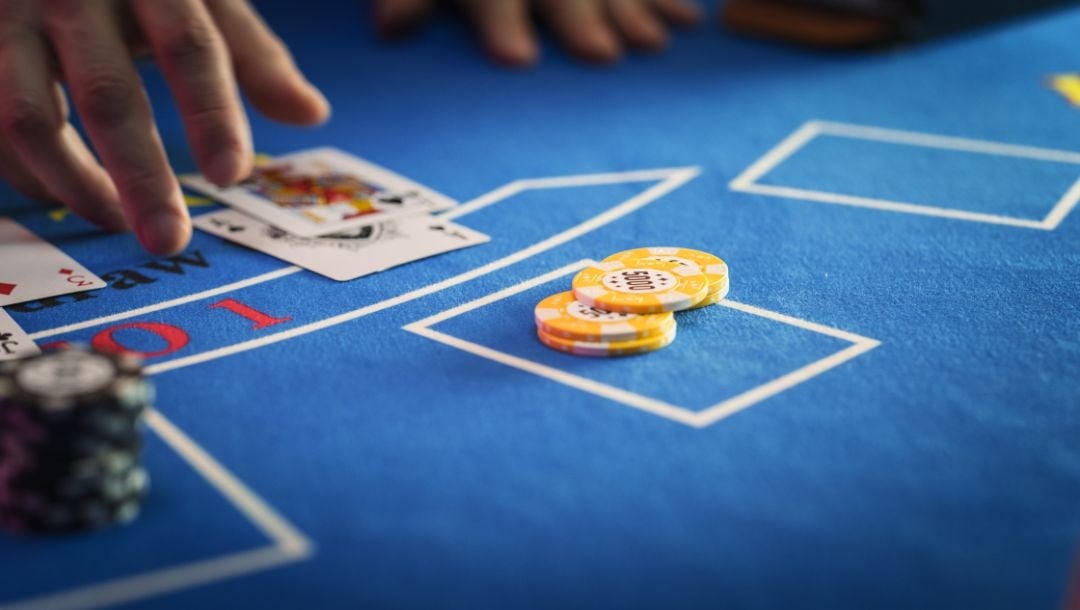 Hands engaged in a game of baccarat, with cards and black and yellow casino chips arranged on the table.