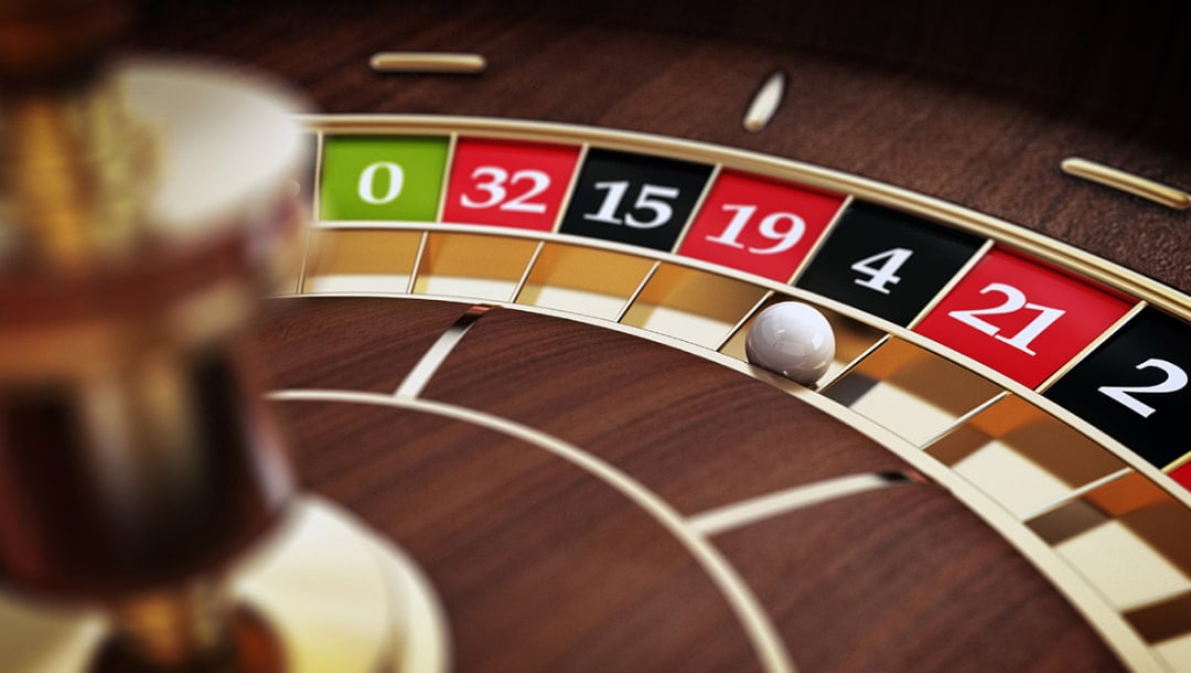 A wooden roulette wheel with green, black, red and gold pockets. There is a white roulette ball in the black number 4 pocket.