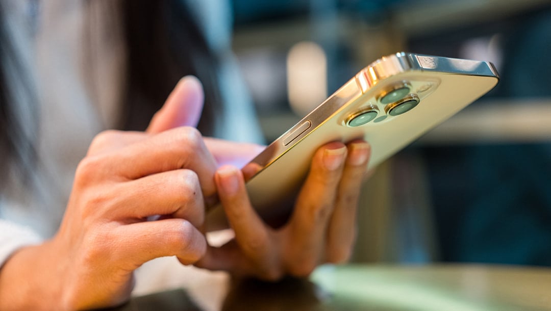 A close up of a woman’s hands with an Apple iPhone device. The woman is scrolling on the iPhone.