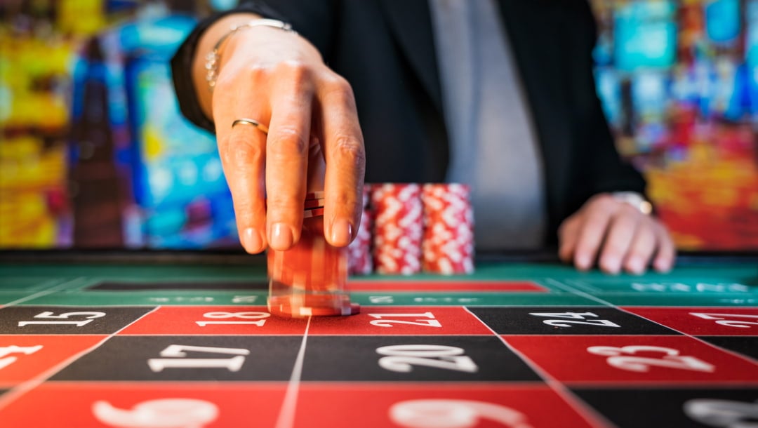 A person placing red casino chips on a roulette table to make a bet.