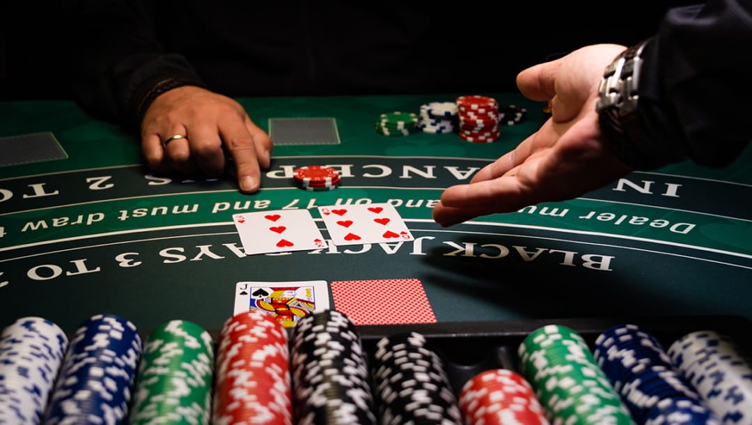 Hands on a green, black and white blackjack table. There is a case filled with casino chips on the table.