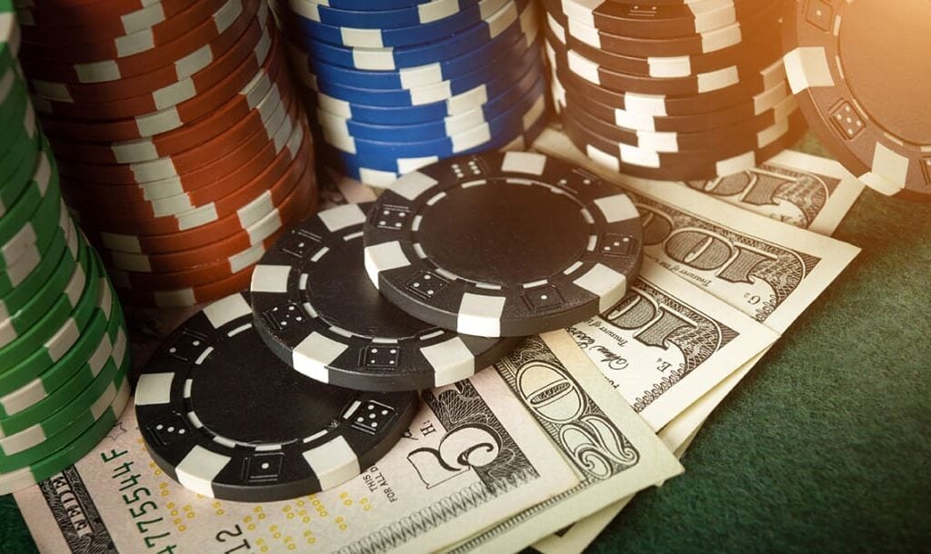 Stacks of green, red, blue, and black casino chips, and a few dollar bills arranged on a poker table.