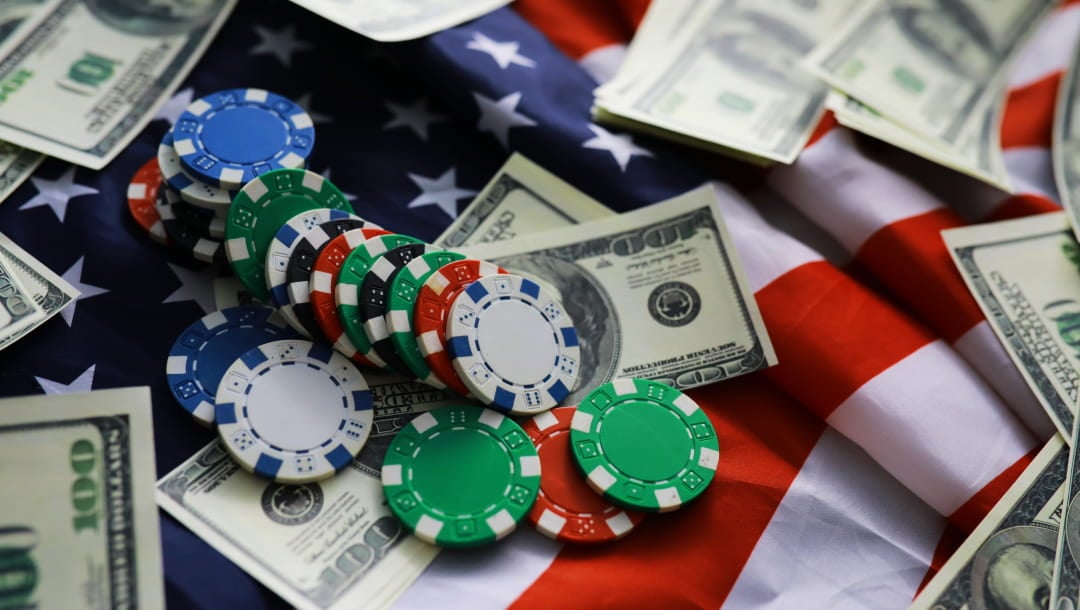 A photograph of white, blue, red, black, and green casino chips and scattered $100 bills on an American flag.